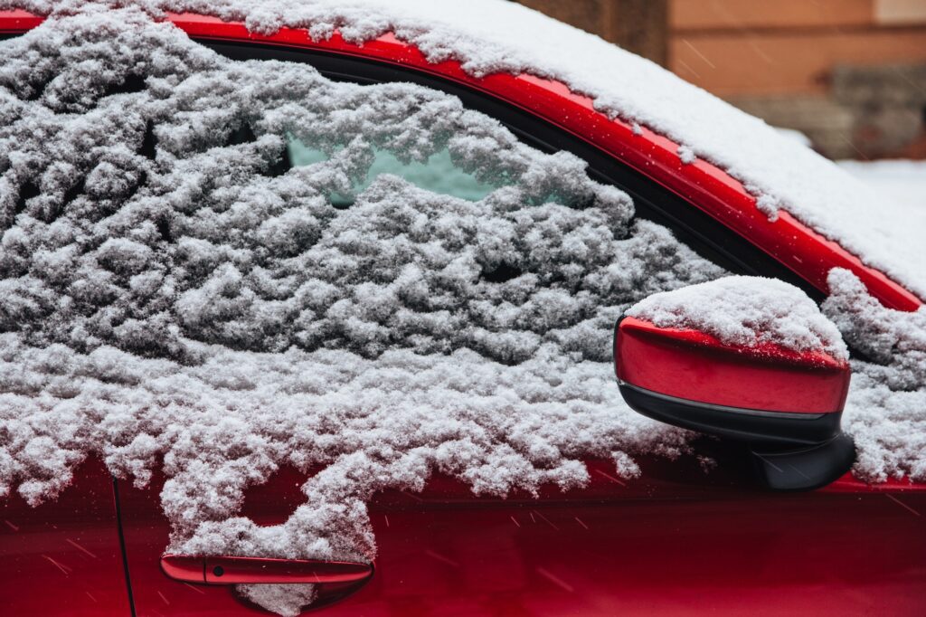 Red car covered with thick snow. Winter blizzard and bad weather conditions